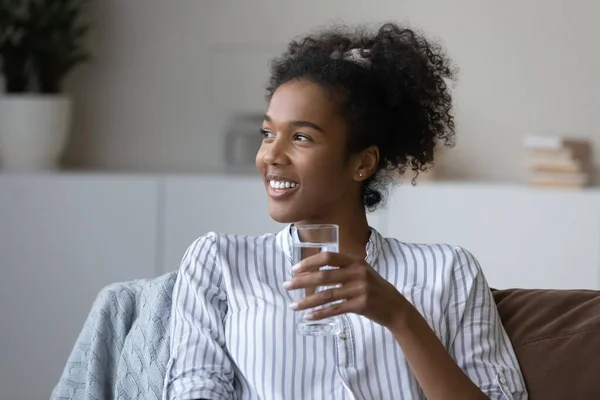 Souriante femme afro-américaine rêveuse tenant un verre d'eau pure — Photo