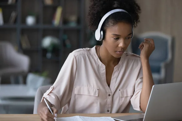 Close up focused African American woman in headphones taking notes — Stock Photo, Image