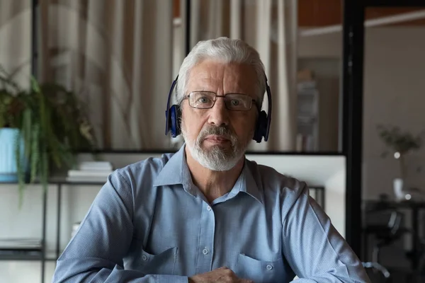 Serious concerned senior 60s male student in headphones and glasses — стоковое фото