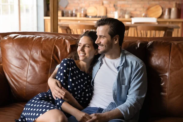 Щаслива молода сімейна пара розслабляється на шкіряному дивані вдома — стокове фото