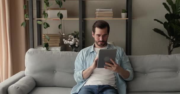 Sorglos glücklicher Millennial-Mann mit Touchpad zu Hause. — Stockvideo