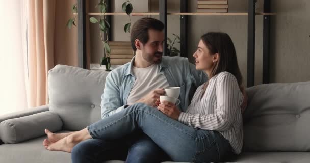 Ευτυχισμένο στοργικό νεαρό οικογενειακό ζευγάρι πίνοντας καφέ στον καναπέ. — Αρχείο Βίντεο
