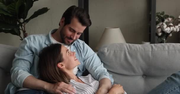 Ευτυχισμένο νεαρό παντρεμένο ζευγάρι που χαλαρώνει στον άνετο καναπέ. — Αρχείο Βίντεο