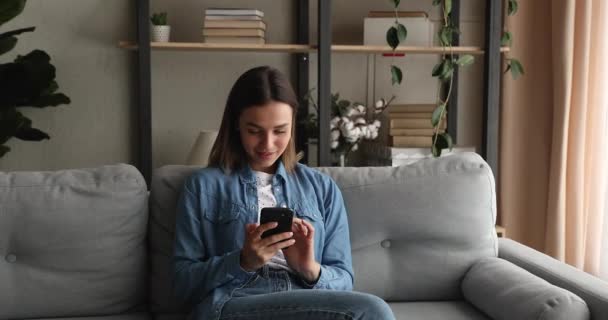 Unbekümmert glückliche junge Frau in den 20ern nutzt Handy zu Hause. — Stockvideo