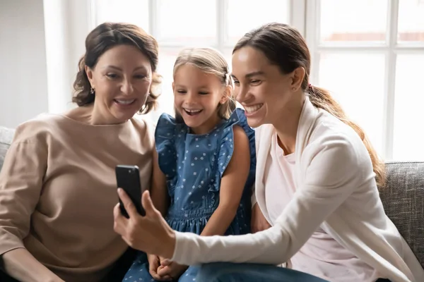 Smiling three generations of women use smartphone — стоковое фото