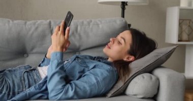 Sakin, rahat bir milenyum kadını. Akıllı telefon kullanıyor, kanepede yatıyor..