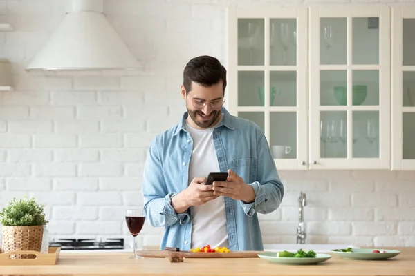 Man cooking in kitchen holding smartphone search recipes on internet