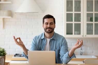 Sakin adam, dizüstü bilgisayarın yanında gözleri kapalı meditasyon yapıyor.