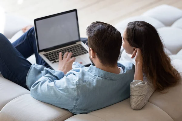 Пара с видом сзади сидят дома на диване с помощью компьютера — стоковое фото