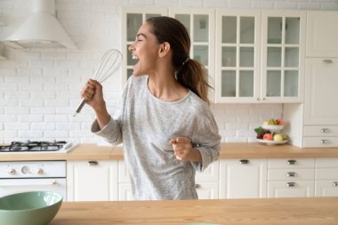 Kadın çırpıcıyı tutuyor, ağzını açıyor ve mutfakta şarkı söylüyor.