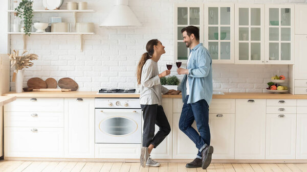 Couple chatting while standing in cozy modern kitchen with wineglasses
