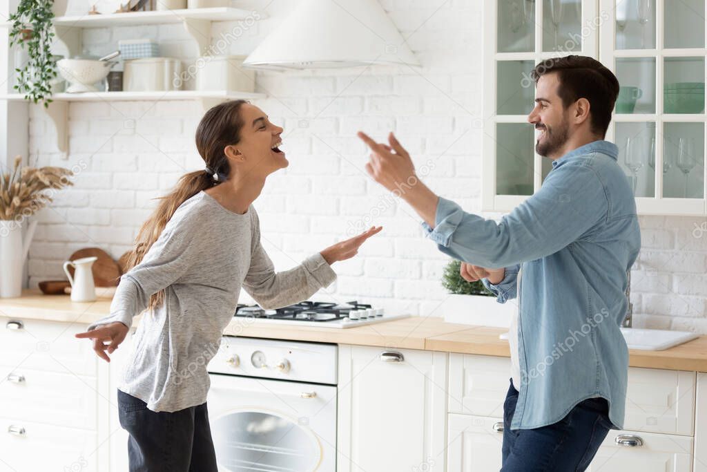 Excited active couple listen music sing dance together in kitchen