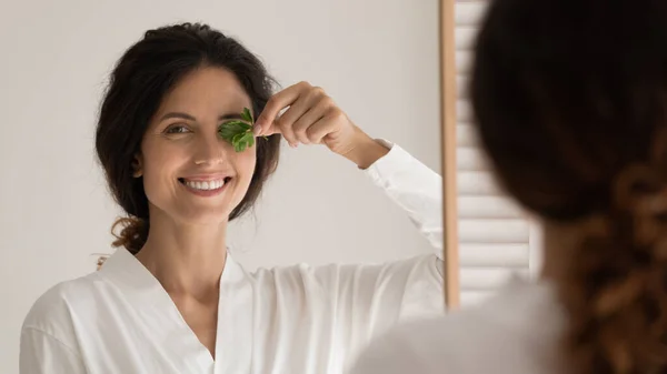Молодая женщина, глядя в зеркало, держит лист петрушки за лицом — стоковое фото