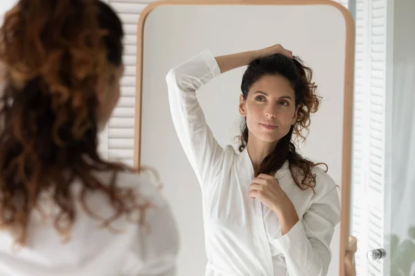 Młoda latynoska kobieta w szlafroku patrząc na lustro tworząc fryzurę — Zdjęcie stockowe