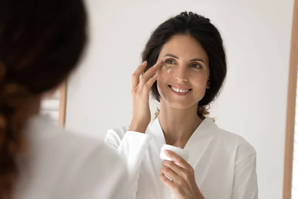 Sorrindo jovem hispânica aplicar creme nutritivo sob os olhos — Fotografia de Stock