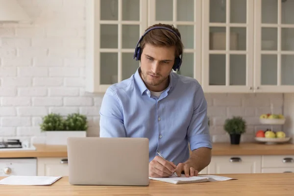 Young male in headset look on pc screen take notes — Stock Photo, Image