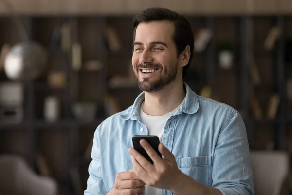 Happy dreamy young man holding smartphone in hands. — Stock Photo, Image