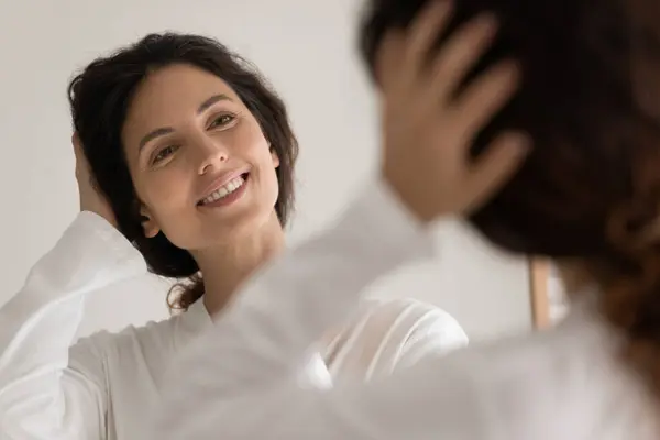Lustro odbicie szczęśliwej młodej kobiety w szlafroku dotykając włosów — Zdjęcie stockowe