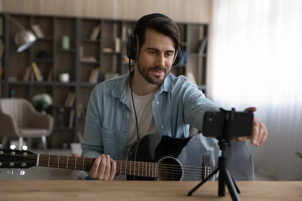 Happy young man in headphones recording video playing on guitar. — Stock Photo, Image
