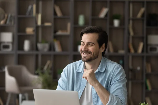 Happy dreamy man looking in distance, distracted from computer work.