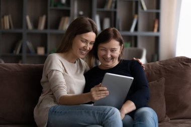 Mutlu, yetişkin bir kız çocuğu tablette yetişkin bir anneye içerik gösteriyor.