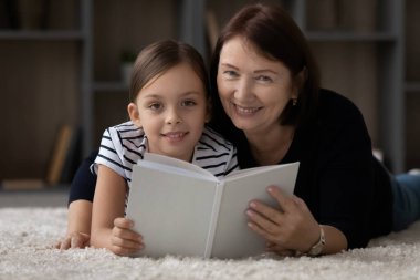 Tatlı çocuk büyükannesiyle kağıt kitap okuyor.