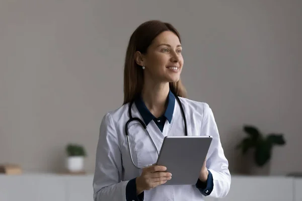 Счастливая вдумчивая женщина-врач, врач с планшетным компьютером в офисе — стоковое фото