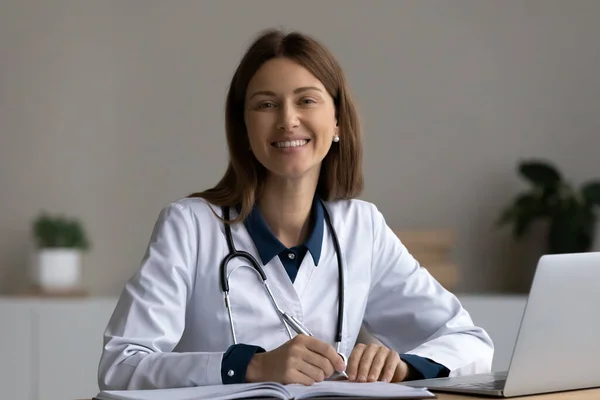Glad säker ung kvinnlig läkare sitter på arbetsplatsen — Stockfoto