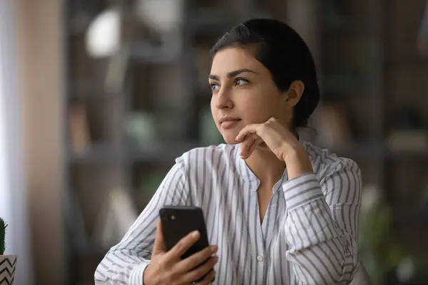 Pensive Indian woman use cellphone thinking planning — Stock Photo, Image