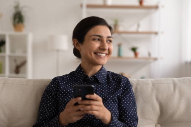 Yakın plan gülümseyen Hintli kadının dikkati akıllı telefondan dağılmış.