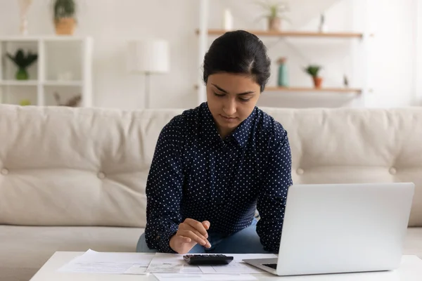 Serious Indian woman calculating expenses, using laptop, sitting on couch — Foto de Stock