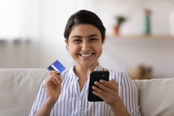 Head shot happy Indian woman holding credit card and smartphone