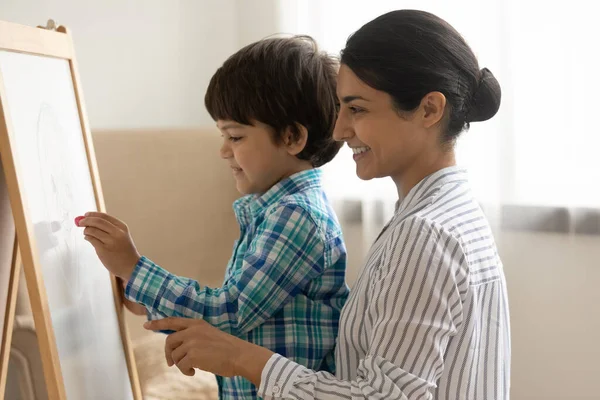 Smiling Indian mother with little son drawing on white board — Photo