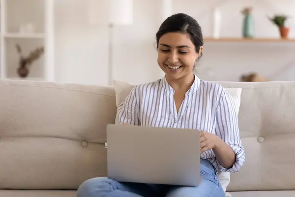 Smiling Indian woman using laptop, having fun, sitting on couch — Stock Photo, Image
