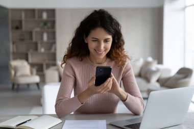 Ofiste gülümseyen Latin kadın cep telefonundan mesaj atıyor.