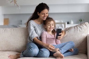 Gülümseyen Latin anne ve küçük kızı cep telefonuyla konuşuyor.