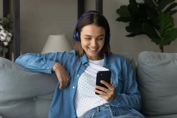 Woman wear wireless headphones smiles looks at cellphone screen — Stock Photo, Image