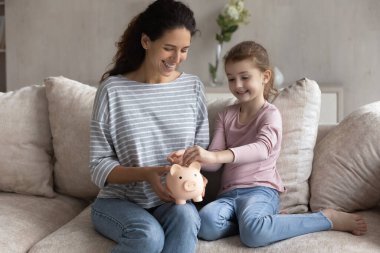 Gülümseyen İspanyol anne ve küçük kızı domuz kumbarasından tasarruf ediyorlar.