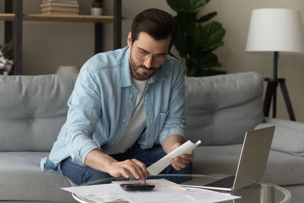 Serious man calculates expenses working sit on sofa at home — Fotografia de Stock