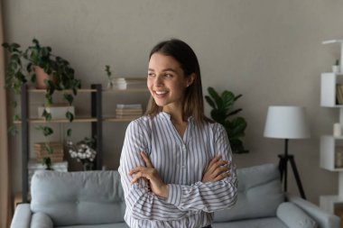 Modern odada kollarını kavuşturmuş bir kadın başka tarafa bakıyor.