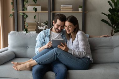 Birbirini seven bir çift, modern tablet cihazıyla kanepeye oturur.