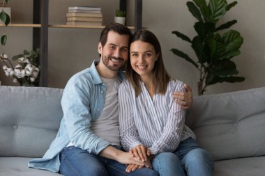 Güzel evli çift kanepeye oturur gülümseyerek kameraya bakar.