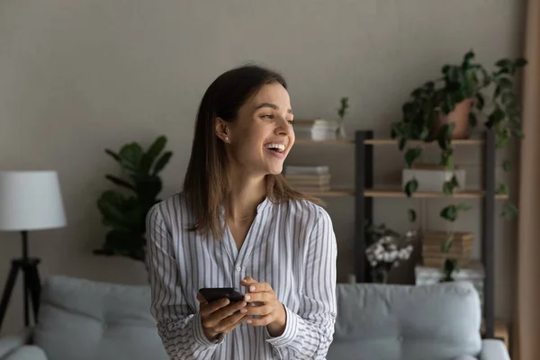 Cheery woman standing in living room with smartphone — Fotografia de Stock