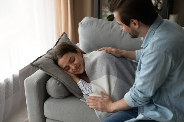 Догляд за чоловіком прикриває сплячий на дивані красива дружина з пледом — стокове фото