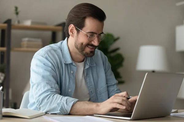 Mężczyzna siedzi przy biurku i pisze smsy na laptopie pracując w biurze. — Zdjęcie stockowe