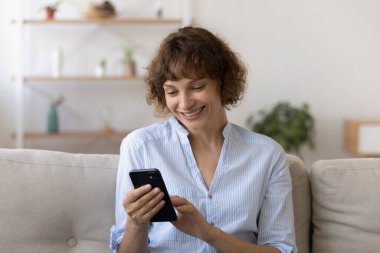 Mutlu, rahat, evde akıllı telefon kullanan genç bir kadın..