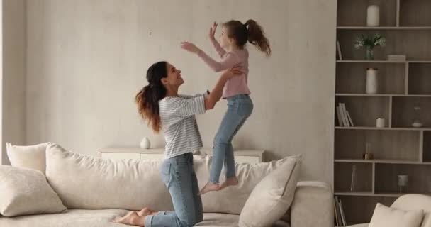 Glada unga mor och dotter har roligt, hoppa på soffan. — Stockvideo