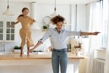 Heyecanlı anne ve küçük kızı modern mutfakta dans ediyorlar.