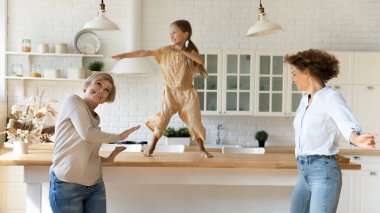 Mutfakta büyükannesi ve annesiyle dans eden küçük mutlu bir kız.