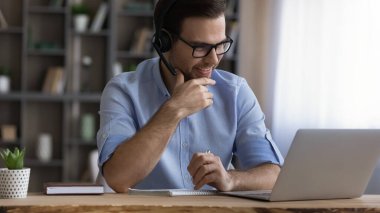 Kulaklık takmış genç bir erkek öğrenci öğretmeniyle internette görüşüyor.